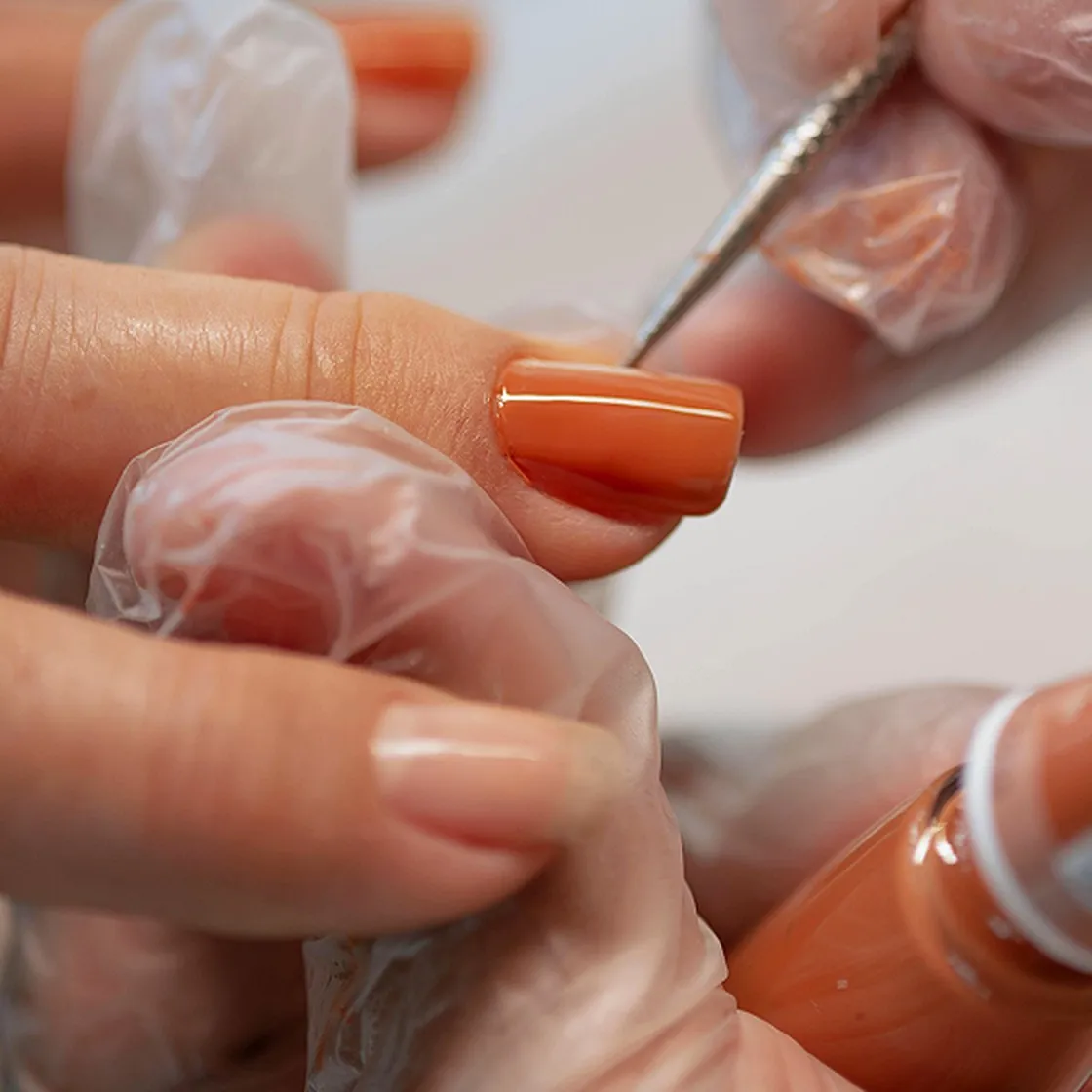 Close-up of orange nail polish being applied during a manicure