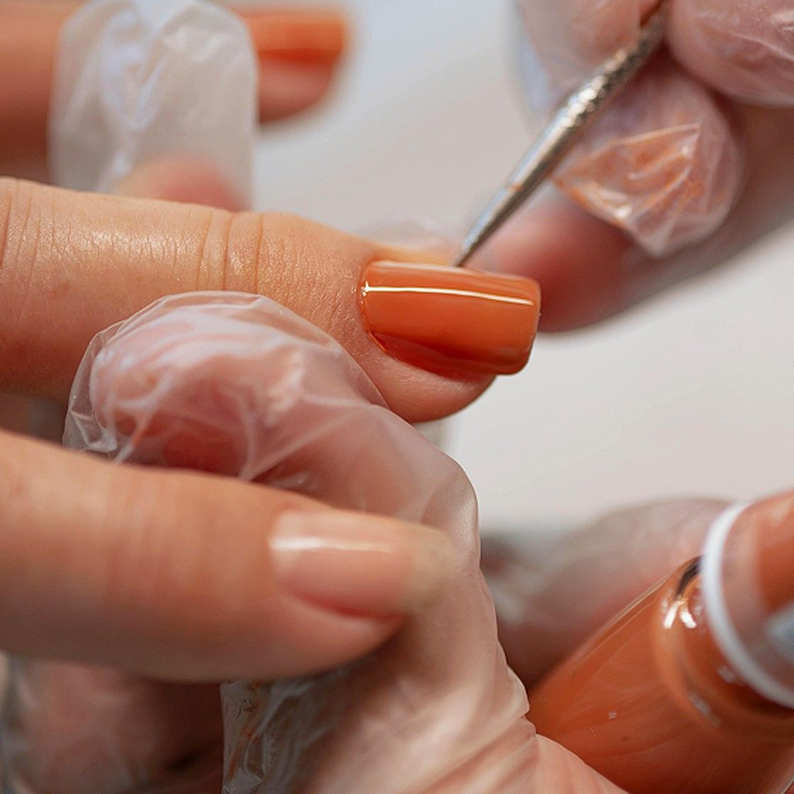 Close-up of orange nail polish being applied during a manicure